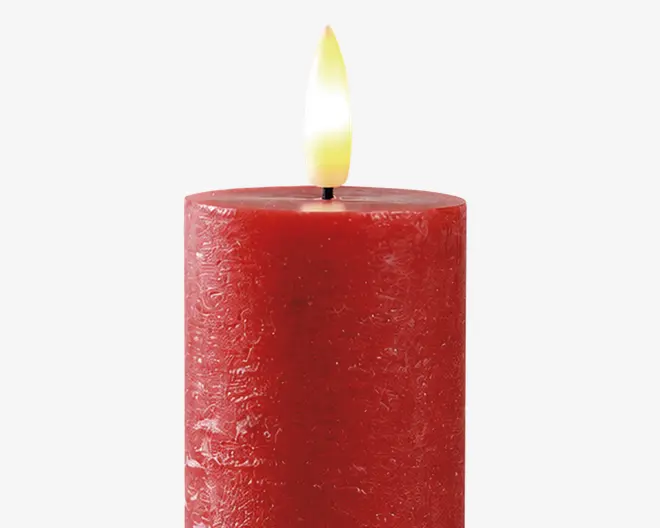 En cylindrisk, dybrød stearinlys med en tekstureret overflade og en glat, flad top. Lyset er tændt med en synlig sort væge og en klar gul-orange flamme. Voksen har en let rustik, ujævn finish, hvilket giver det et håndlavet udseende.
