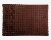 Rektangulært brunt tæppe med en blød, plysset tekstur og et diskret ternet mønster. Overfladen har hævede, tuftede sektioner langs den ene kant, hvilket giver ekstra dimension og komfort. Tæppet er ensfarvet og designet til en hyggelig, indbydende fornemmelse.