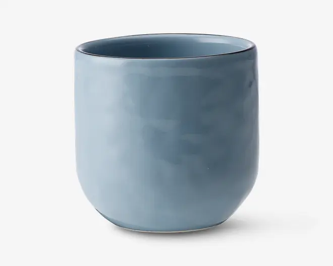 En glat, cylindrisk kop med mat blå finish. Koppen har en let afrundet bund og en tynd kant uden hank. Overfladen er jævn, og farven er ensartet, hvilket giver et moderne og minimalistisk udtryk.