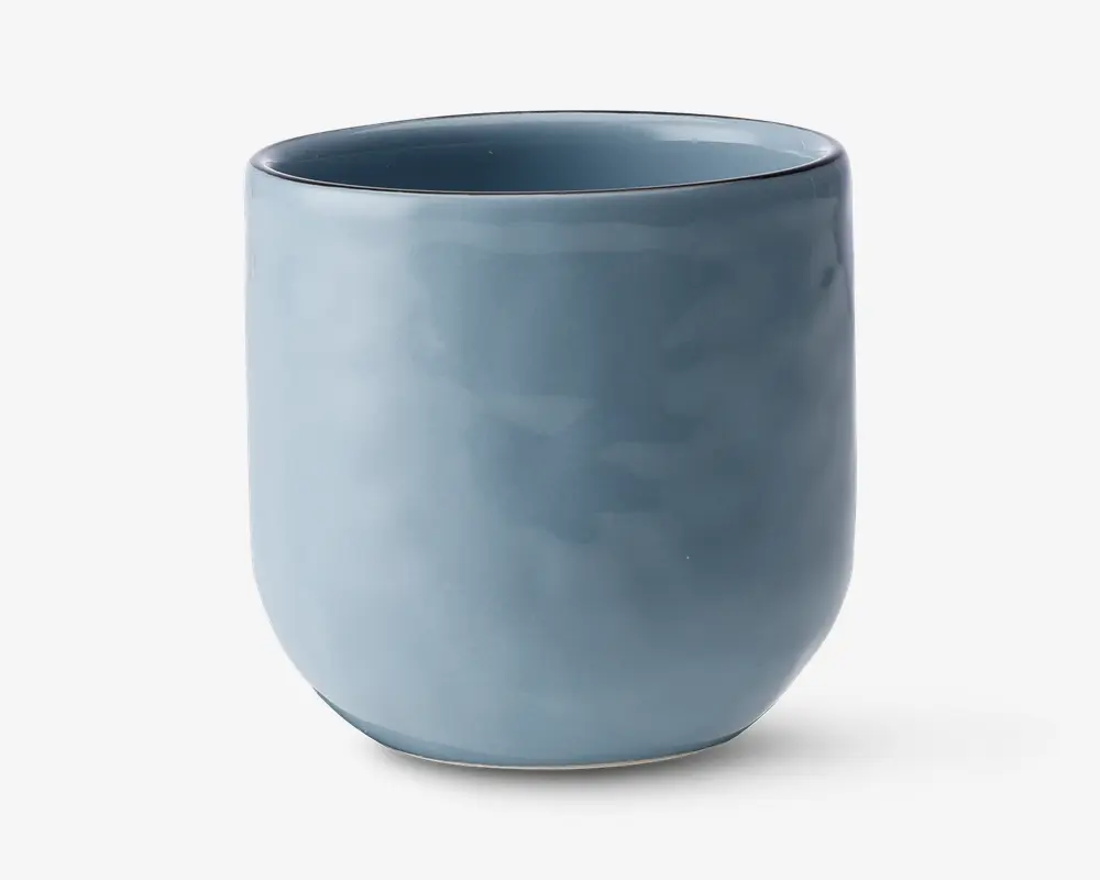 En glat, cylindrisk kop med mat blå finish. Koppen har en let afrundet bund og en tynd kant uden hank. Overfladen er jævn, og farven er ensartet, hvilket giver et moderne og minimalistisk udtryk.