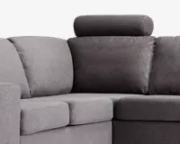 Nærbillede af hjørnet på en modulsofa med to forskellige grå nuancer i betrækket. Sæde- og ryghynderne er tykke og bløde, hvilket giver god komfort. Den ene sektion har en nakkestøtte for ekstra støtte til nakken. Stoffet ser tæt vævet ud og giver et moderne og slidstærkt udtryk.