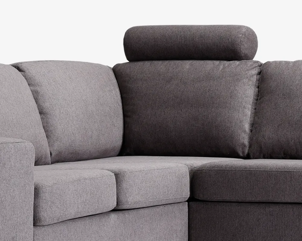 Nærbillede af hjørnet på en modulsofa med to forskellige grå nuancer i betrækket. Sæde- og ryghynderne er tykke og bløde, hvilket giver god komfort. Den ene sektion har en nakkestøtte for ekstra støtte til nakken. Stoffet ser tæt vævet ud og giver et moderne og slidstærkt udtryk.