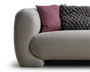 Nærbillede af en lysebeige polstret sofa med afrundet armlæn, stylet med en støvet lilla pude og en mørk, kraftigt strikket pyntepude.