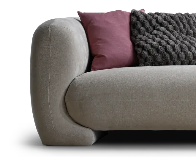 Nærbillede af en lysebeige polstret sofa med afrundet armlæn, stylet med en støvet lilla pude og en mørk, kraftigt strikket pyntepude.